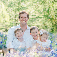 Father and children wearing white snuggled together in a field o f flowers in Dallas.