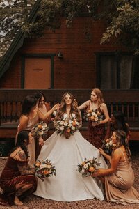 A person on their wedding day is surrounded by their wedding party as they prepare for their wedding at Cabins Strawberry Hill in Arizona. The individual, dressed in a flowing white gown, is the center of attention as the others hold bouquets.