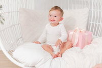 baby boy sitting in a cozy egg chair with a present by miami christmas mini session photographer msp