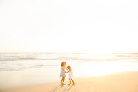 Family Photographer, two girls hold hands on the beach