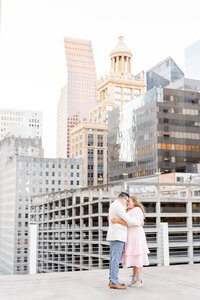 Future bride and groom hugging and forehead to forehead on rooftop parking garage with Downtown Houston in the background
