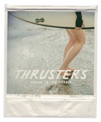 female surfer holding a surfboard with feet in the sand and a logo for Thrusters Surf Shop