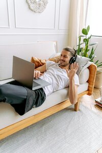 man laying on couch smiling and waving at computer