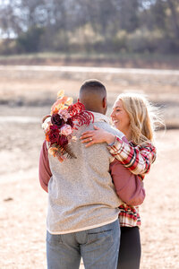 man and woman standing in a field smiling and embracing with beautiful bouquet