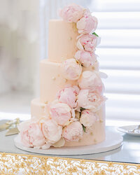 three tiered pink wedding cake bedecked with pink peonies and gold dots