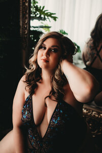 Beautiful plus size beauty sitting in front of mirror in boudoir studio wearing lingerie from Savage XFenty
