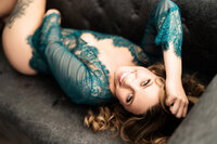 smiling woman laying on couch hand in hair in emerald green lace long sleeve lingerie