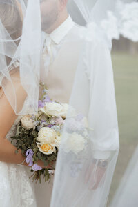 Bride and groom portrait under a bridal veil with a flower bouquet
