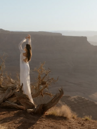 Bride posing at sunrise in the Moab desert with her long sleeve lace Claire Pettibone gown.