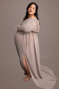 Pregnant mother wearing a light brown dress and she is looking over her shoulder for the photo.