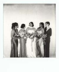 Black and white Polaroid photo of a bride and her bridesmaids laughing together in a studio setting — an editorial bridal party portrait made by a film wedding photographer.