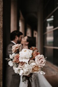 Bride and groom kissing behind wedding flower bouquet