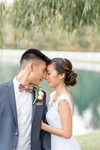 Bride holding onto Groom's left arm as they smile with eyes closed and touch their foreheads together.