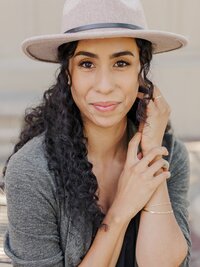Woman smiling with a tan hat posing with arms near her face — NYC brand photography shoot.