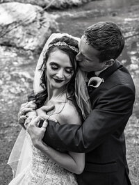 Black and white wedding portrait of a couple standing beside a river during their Colorado wedding.