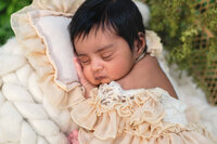 dark haired baby girl in beige frilly dress sleeping in outdoor session.