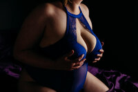closeup of a woman in bright blue bodysuit holding her chest and she kneels on purple sheets for her Wisconsin boudoir photography session
