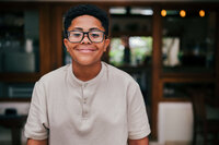 Individual boy with glasses and smiling with a tan shirt