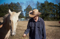 Same sex inner racial cowboy couple hold each other in a field.