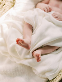 A close-up of a baby's feet as the baby is wrapped in a white blanket during a Richmond newborn photography session by Katie Stansfield Photography.