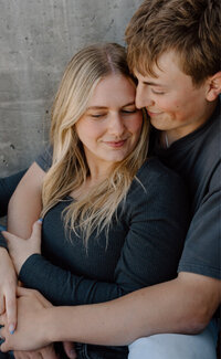 Close up of a man holding his girlfriend. Both are sitting on the ground and neither are looking at the camera.
