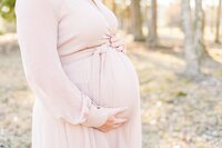 Close up of a woman in pink dress holding her baby bump at the top and bottom