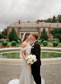 Film photo of a bride and groom kissing in front of the fountain at the Massachusetts Horticultural Society’s Garden at Elm Bank during their summer wedding — captured by a film wedding photographer.