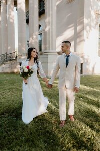 Couple wearing wedding dress and suit walking holding hands.