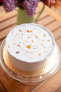 lavendar sweet heather anne cake on class stand with flowers in the background during styled shoot