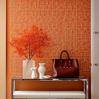 Modern console table with vases, a leather handbag, and orange foliage against a geometric orange accent wall.