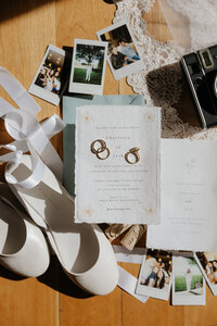 A bottle of champagne, rings, and wedding invitations laid out together 