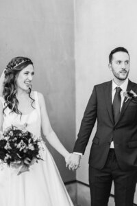A wedding couple holding hands as one also holds a bouquet of flowers 