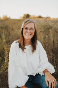 Picture of Jennifer who is smiling, has long brown hair and glasses with a field in the background.