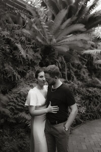 Black and white photo of a couple embracing in a lush tropical garden during their engagement session, photographed by Rainstorm Photo & Video in a calm, cinematic documentary style.