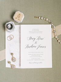 sage and white wedding invitations laid out next to stamp and braclet
