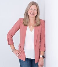 Maureen in pink blazer and jeans with hand on hip smiling at camera