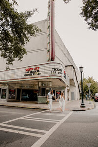 Couple wearing all white and crossing the street in front of an old theater
