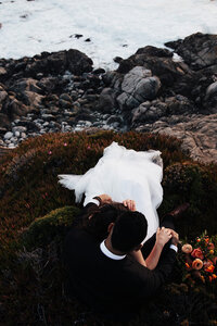 bride leaning on groom sitting at cliff
