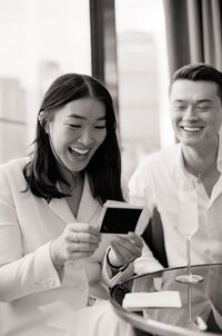 The bride and groom grin at receiving their elopement day Polaroids in Boston -- candid black and white film photography. 