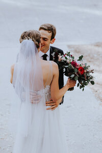 Wedding Photographer, newly married husband and wife kiss, she holds her bouquet