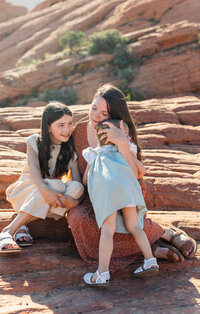 mom sitting on red rocks in snow canyon state park and cuddling with her two girl s