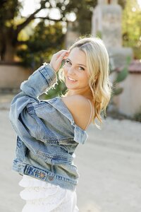girl smiling with a denim jacket and white dress for her senior pictures in Santa Clarita California