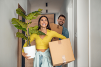 Happy couple smiling holding boxes and a plant while moving out of their Edmonton home after an eco-friendly move-out cleaning by Fresh Nest Green Cleaning