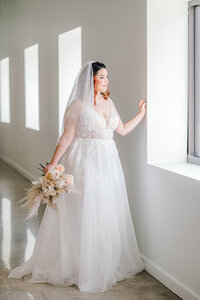 bride stands in front of a window at Benson District Loft  in Omaha