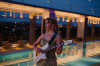 a woman playing a guitar outside by the water and lights