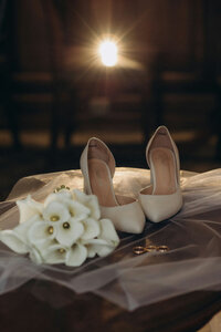Bridal heels, bouquet, and veil softly lit in a moody setting