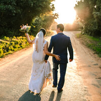 A couple walking on a dirt road while the bride holds up her bouquet, holding her partner's bum.