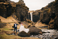 Couple navigating their path against a beautiful waterfall as backdrop during their Iceland elopement.