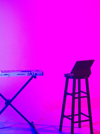 Neon-lit stool and synth keyboard against a black backdrop – artistic set detail for musician brand shoots by Mewphotovideo