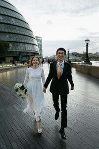 A bride and groom walk across a lawn in a documentary-style black and white photo.